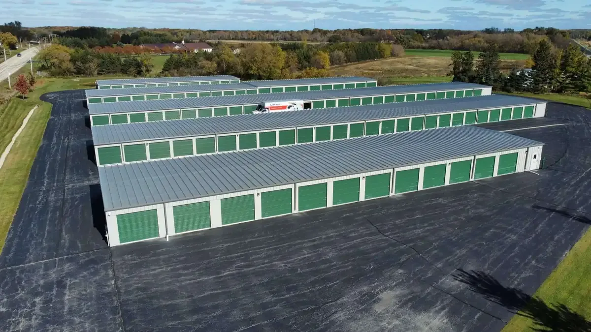 Aerial view of a large storage facility with multiple rows of self-storage units with green doors and metal roofs,...