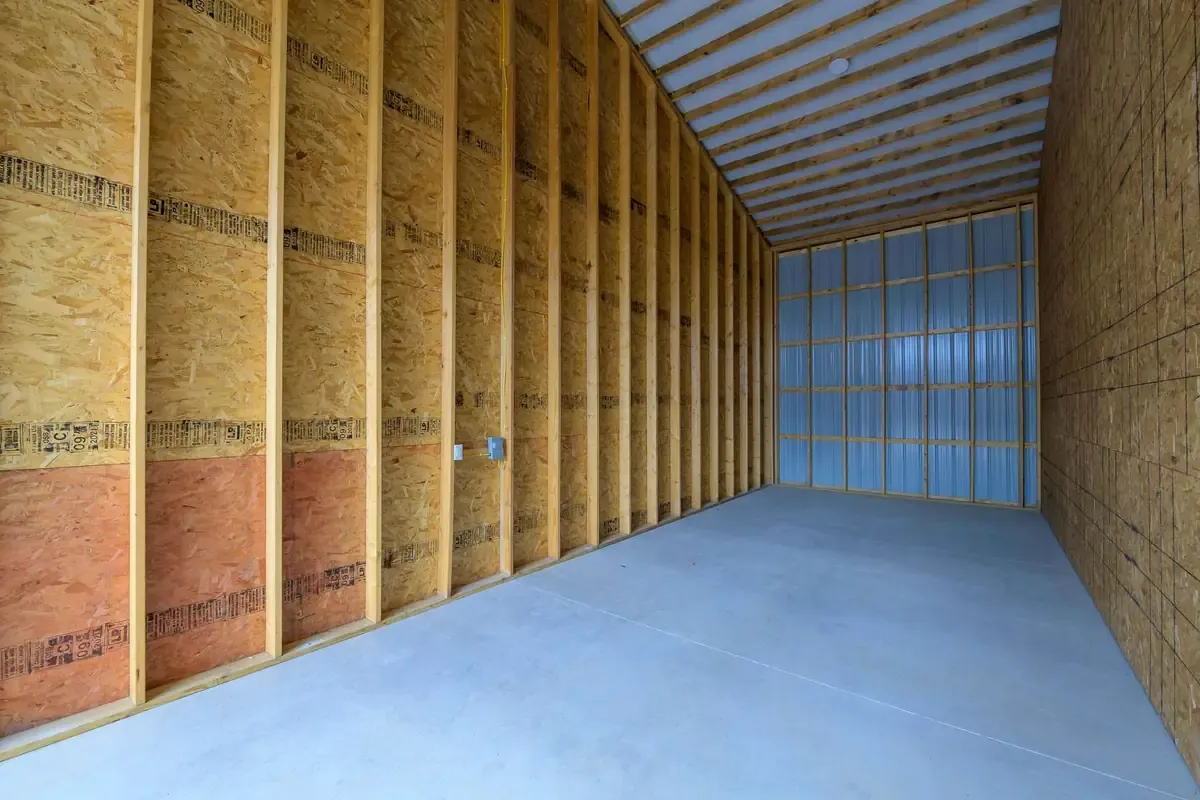 Interior of an unfinished storage unit with exposed wooden framing, OSB walls, and a metal roof.